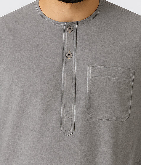 Man wearing an ash grey traditional thawb with round neckline, button placket, and chest pocket, standing against a light neutral background, showcasing modest Islamic menswear.