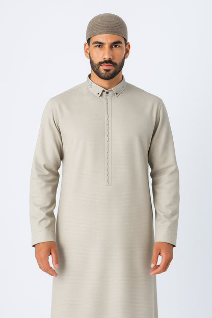 Man wearing a stone beige thobe with embroidered collar and button placket, standing against a white studio background, showcasing modest Islamic fashion.