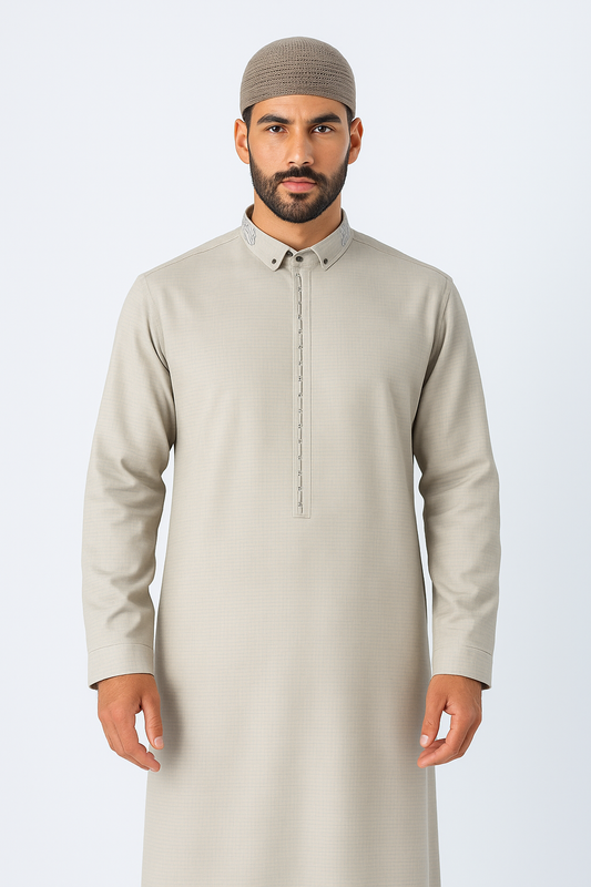 Man wearing a stone beige thobe with embroidered collar and button placket, standing against a white studio background, showcasing modest Islamic fashion.