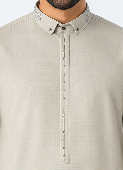 Man wearing a stone beige thobe with embroidered collar and button placket, standing against a white studio background, showcasing modest Islamic fashion.