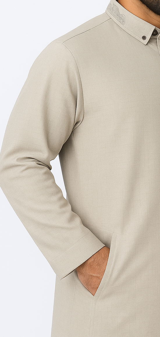 Man wearing a stone beige thobe with embroidered collar and button placket, standing against a white studio background, showcasing modest Islamic fashion.