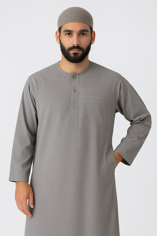 Man wearing an ash grey traditional thawb with round neckline, button placket, and chest pocket, standing against a light neutral background, showcasing modest Islamic menswear.